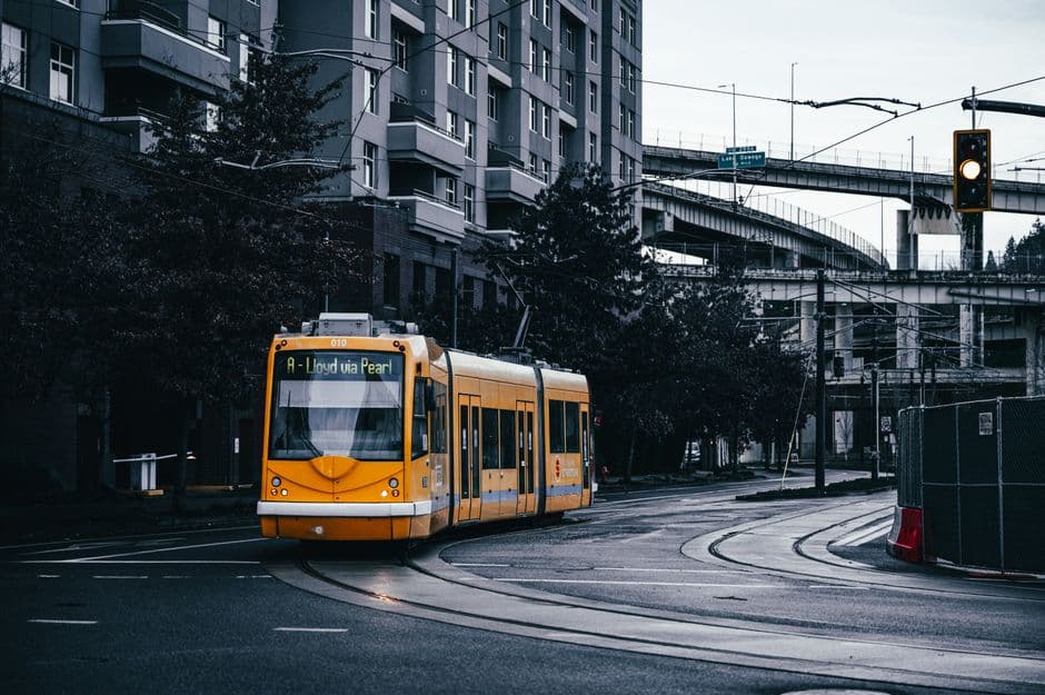 An orange Portland Streetcar signed A, Lloyd via Pearl, turning on a wet street beside an apartment building and a highway overpass