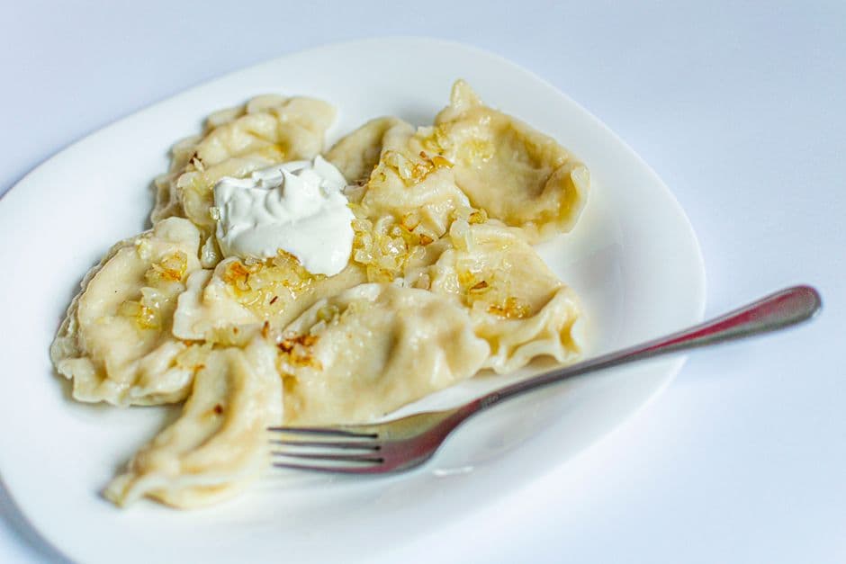 A plate of Polish pierogi with caramelized onions and a spoonful of sour cream, the dish every Krakow restaurant is judged on