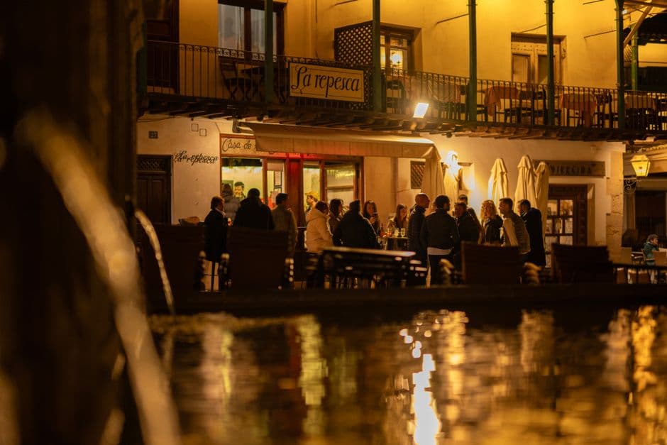 People eating and drinking outside a bar on a lamplit square at night, the way Gracia does dinner