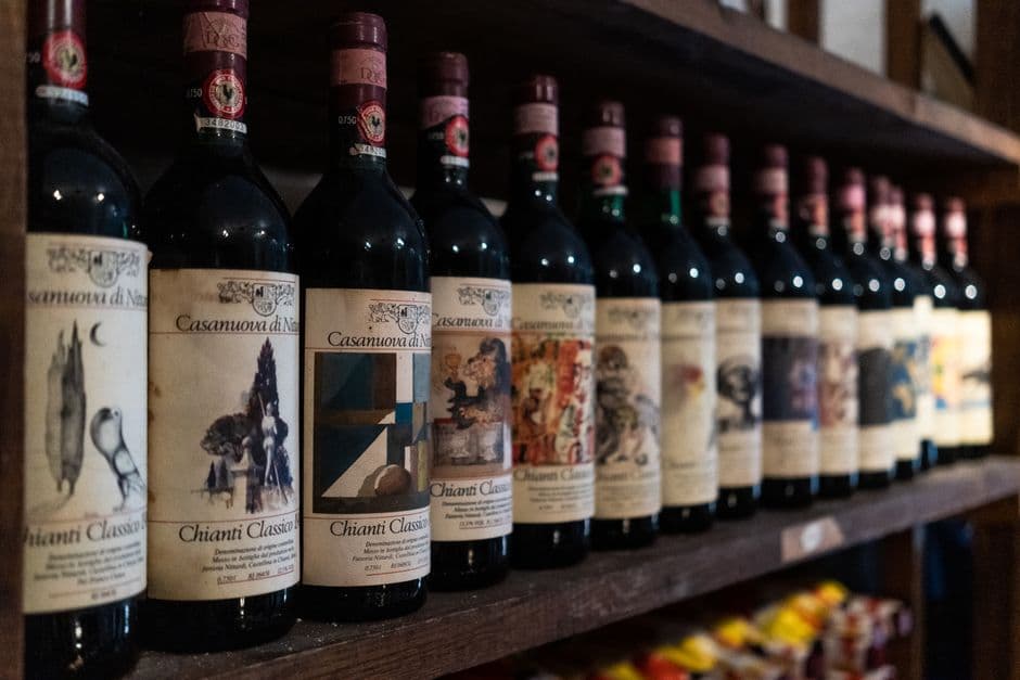 A row of Chianti Classico bottles standing on a dark wooden shelf, labels facing out, receding into shallow focus