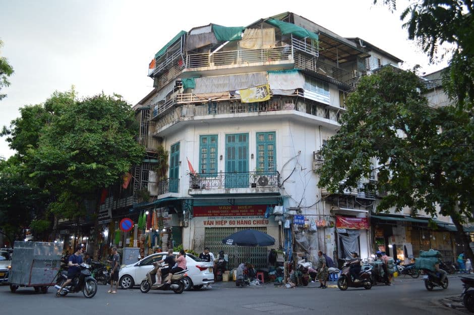 A street corner in Hanoi's Old Quarter with shopfronts, parked motorbikes and low plastic stools on the pavement