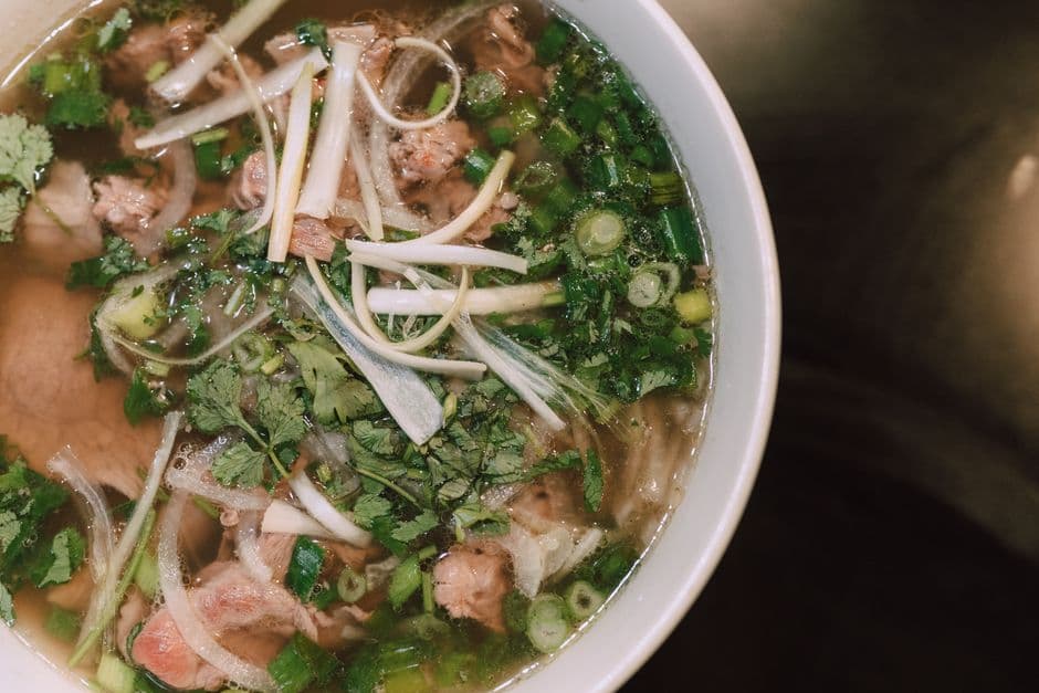 A bowl of Vietnamese pho with sliced beef, rice noodles, spring onion and coriander, seen from above