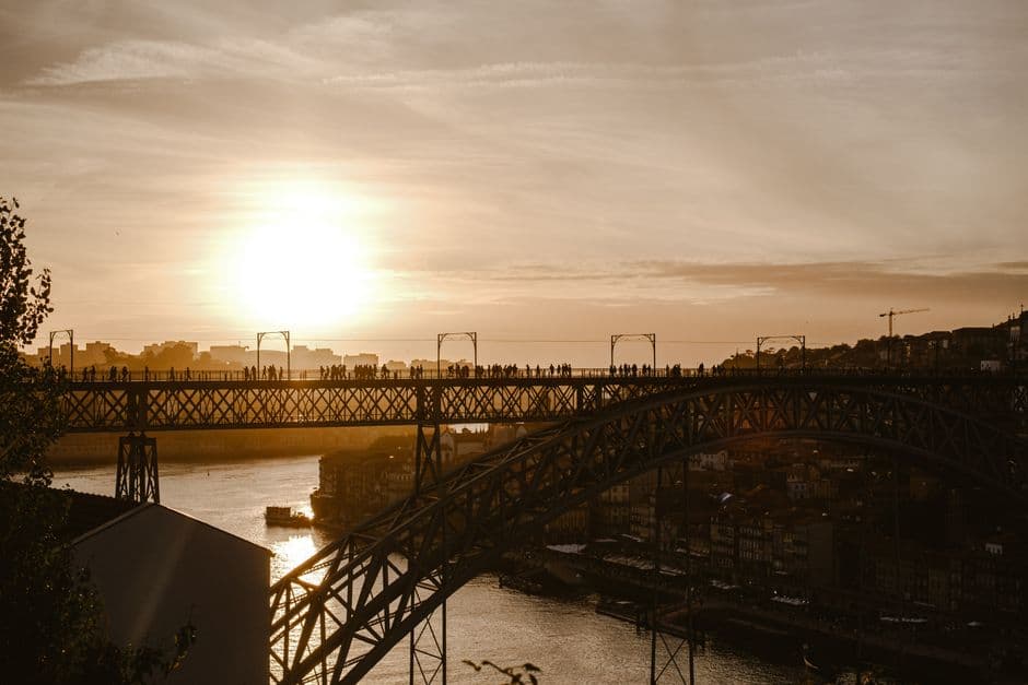 Silhouette of pedestrians crossing the upper deck of the Ponte Dom Luis I over the Douro at sunset, with the Ribeira waterfront below