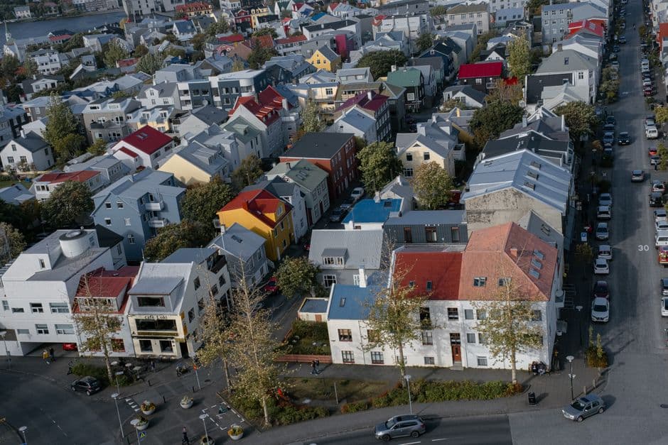 A high view over the colored tin roofs of central Reykjavik, looking down a street lined with parked cars toward the sea