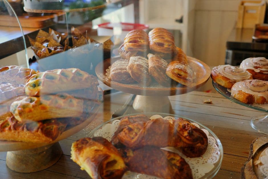 Pastries, cinnamon buns and danishes arranged on cake stands behind the glass counter of a bakery