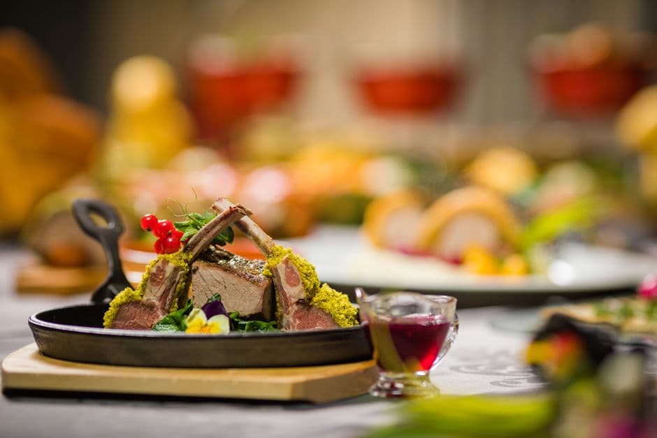A rack of lamb with a green herb crust, sliced and served in a small cast iron pan with redcurrants and a jug of dark sauce