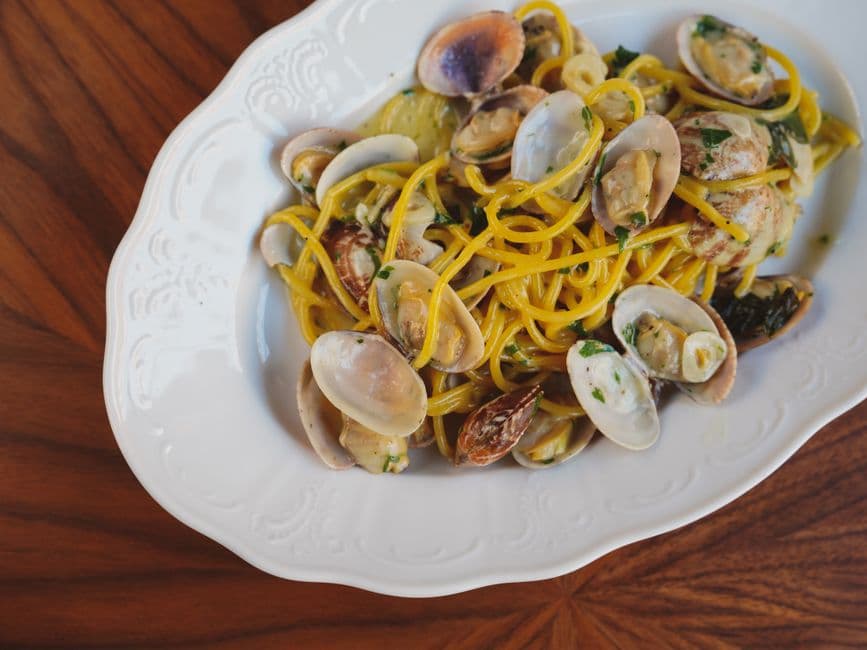 An overhead view of a white ceramic plate of yellow spaghetti tossed with clams in their shells and chopped parsley