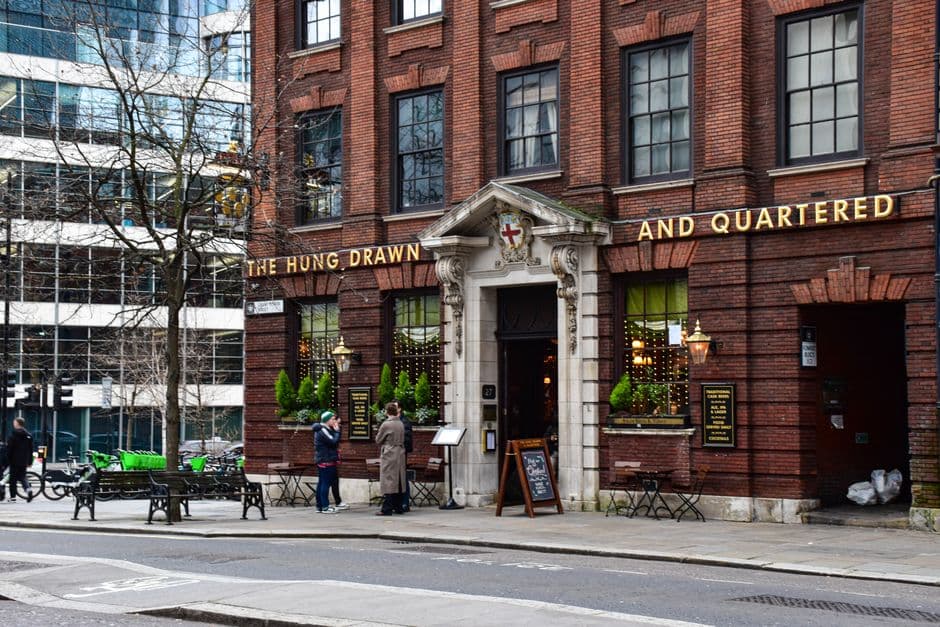 The front of a traditional London pub in red brick, with a stone portico, gold lettering across the facade and lanterns either side of the door