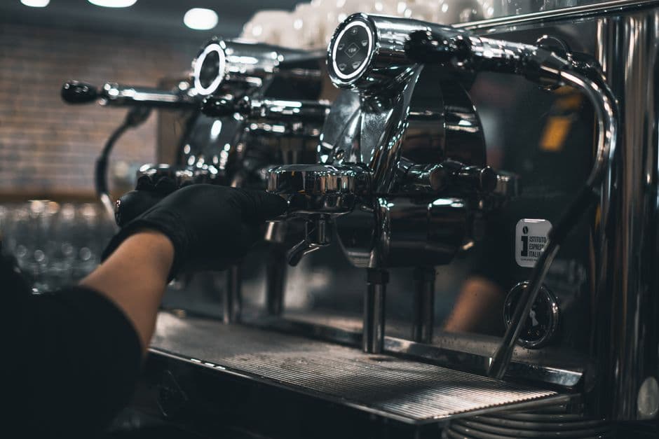 A gloved hand locking a portafilter into a polished chrome espresso machine, with an Istituto Espresso Italiano sticker on its side