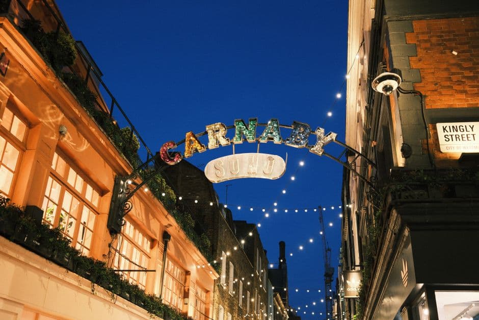 The illuminated Carnaby arch spelling SOHO at dusk, with a Kingly Street sign mounted on the building to the right