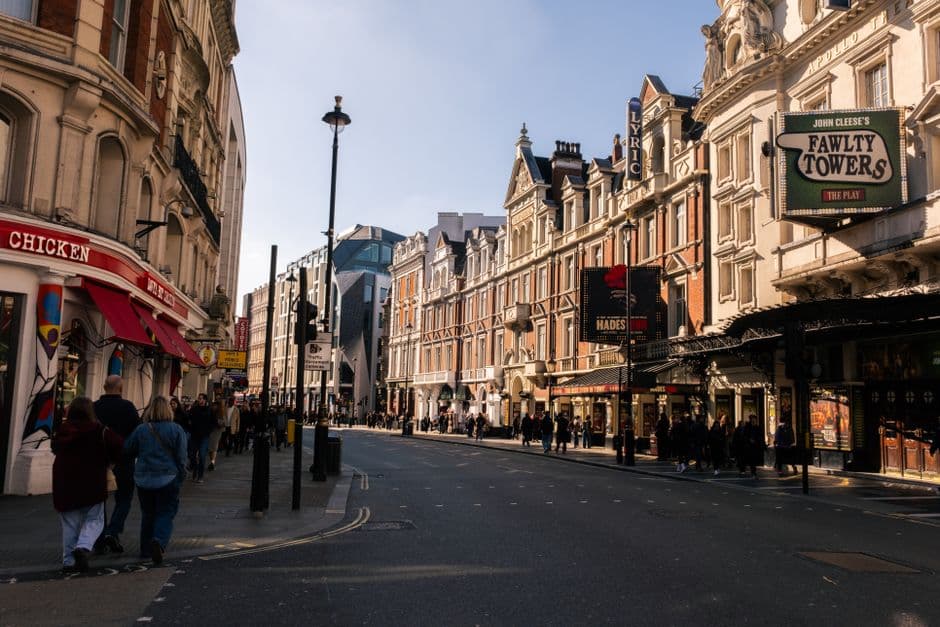 Shaftesbury Avenue in low afternoon sun, with the Lyric and Apollo theatre frontages and their illuminated show marquees along the right side of the street