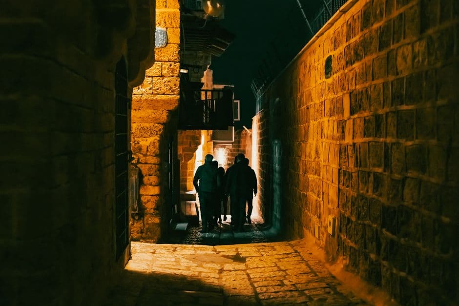 A narrow stone alley in Old Jaffa lit at night with three people walking away from the camera