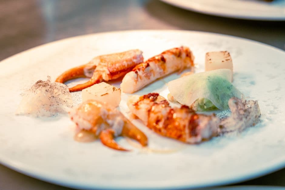 A fine dining plate of langoustine, scallop and shellfish with a light foam, the shape of a Nordic tasting menu course