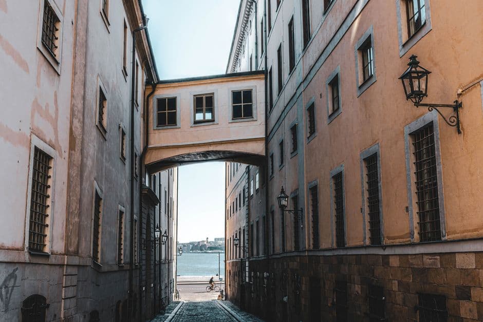 A narrow lane between tall buildings in central Stockholm sloping down to open water at the end