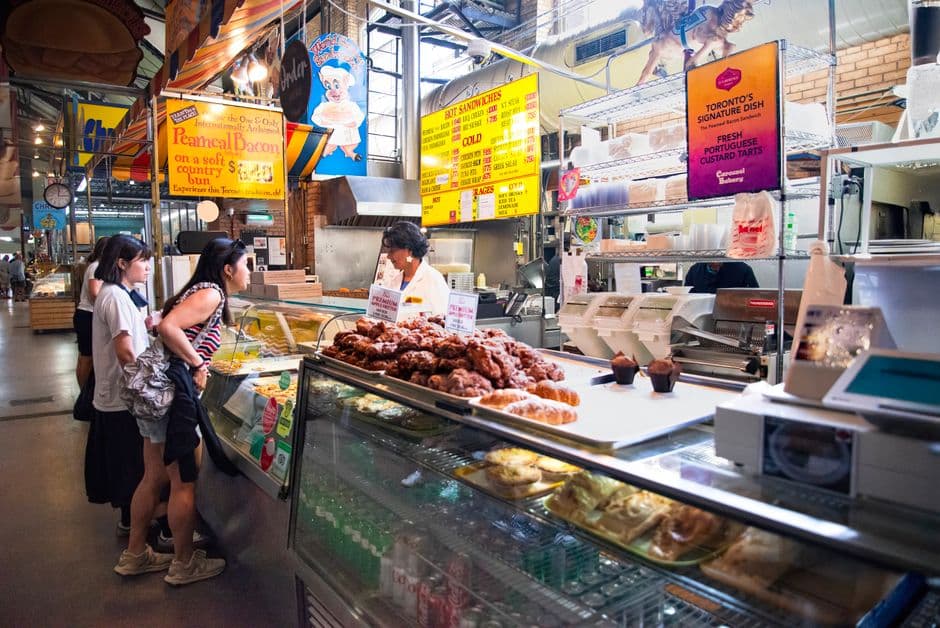 The Carousel Bakery counter inside St. Lawrence Market in Toronto, with signs for peameal bacon on a soft country bun and customers ordering