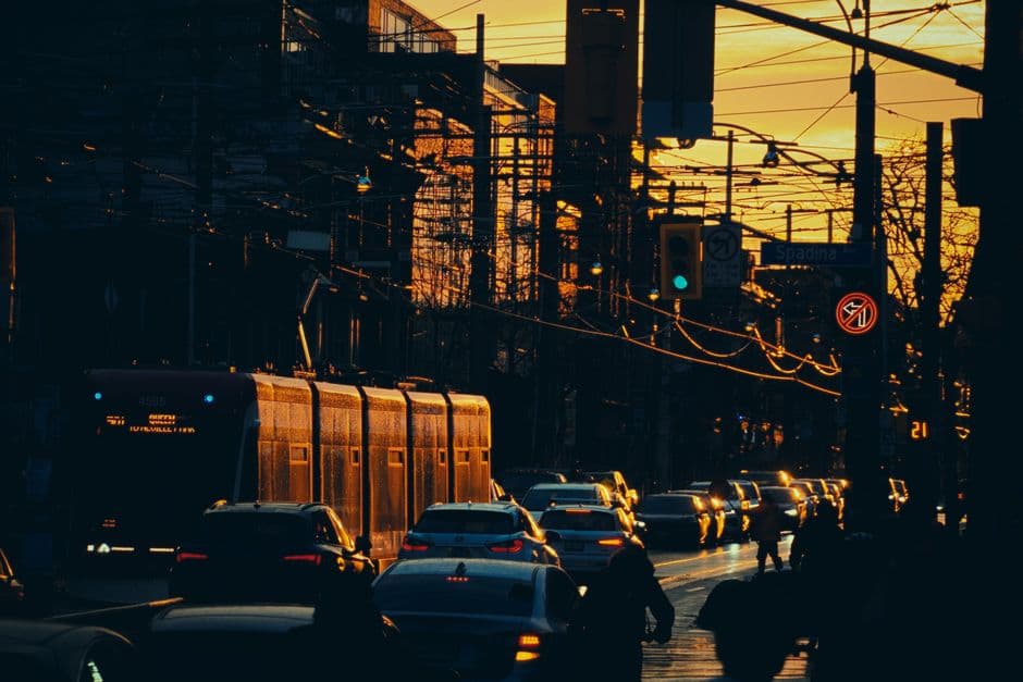 A streetcar in evening traffic in Toronto at sunset, with a Spadina Avenue street sign overhead