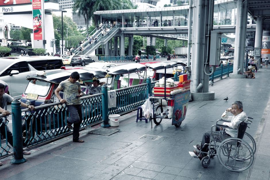 Tuk-tuks parked along a Bangkok sidewalk in the afternoon beside a food cart with nobody working it, during the gap between the lunch and evening street food shifts