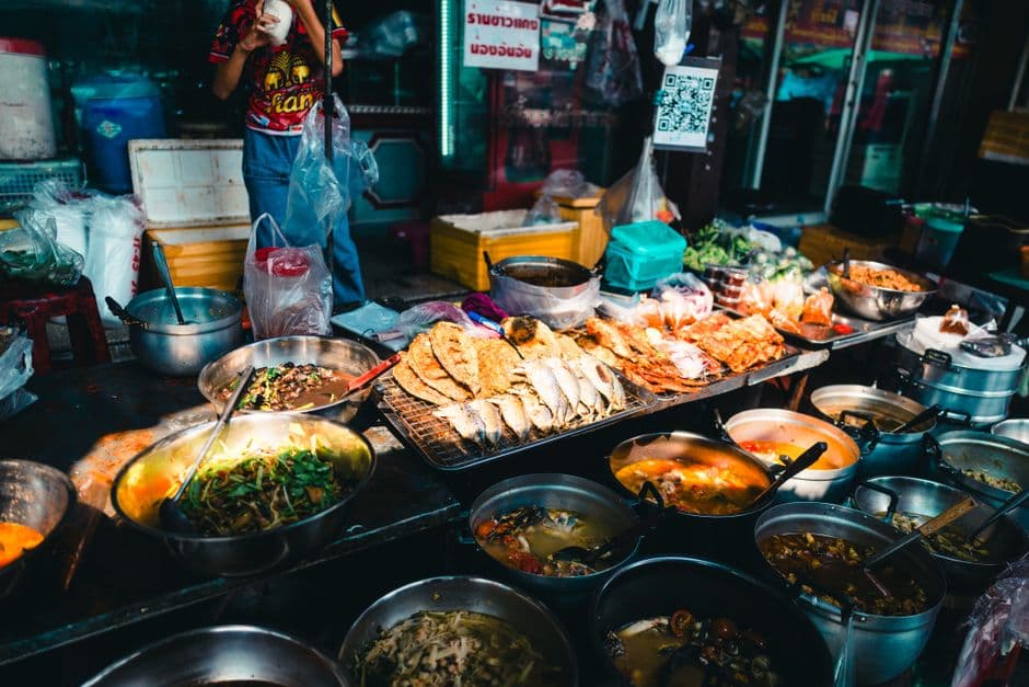 A Thai khao gaeng stall with metal pots of curries and soups and a rack of grilled fish, the rice and curry format that dominates Bangkok street food at lunch