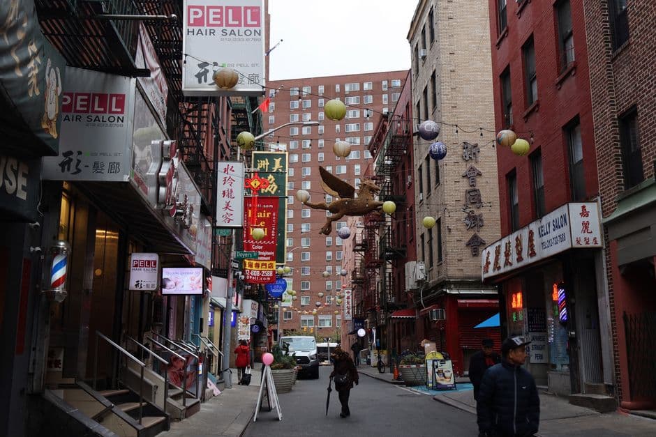 Pell Street in Manhattan's Chinatown, with bilingual shop signs, a 22 Pell St hair salon sign, red brick buildings and paper lanterns strung across the street