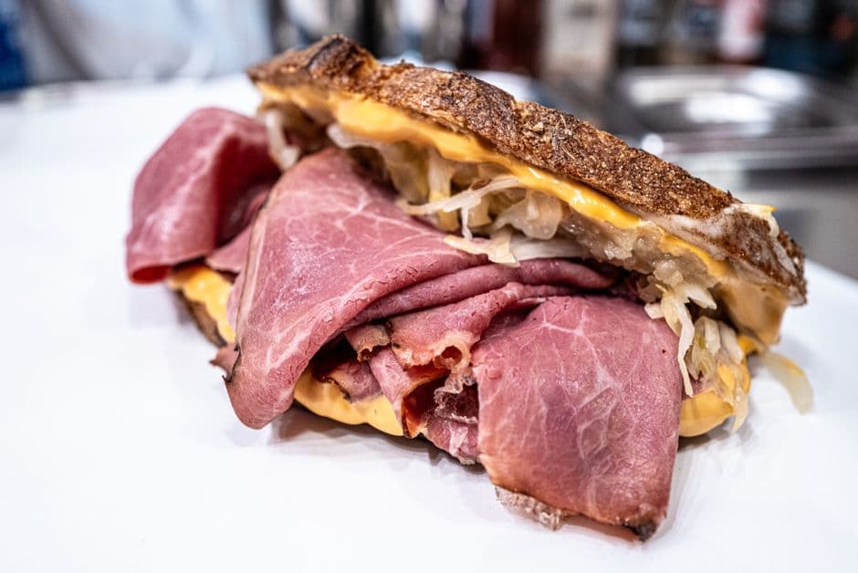 A deli sandwich of thinly sliced cured beef with sauerkraut and melted cheese on toasted bread, on a white counter