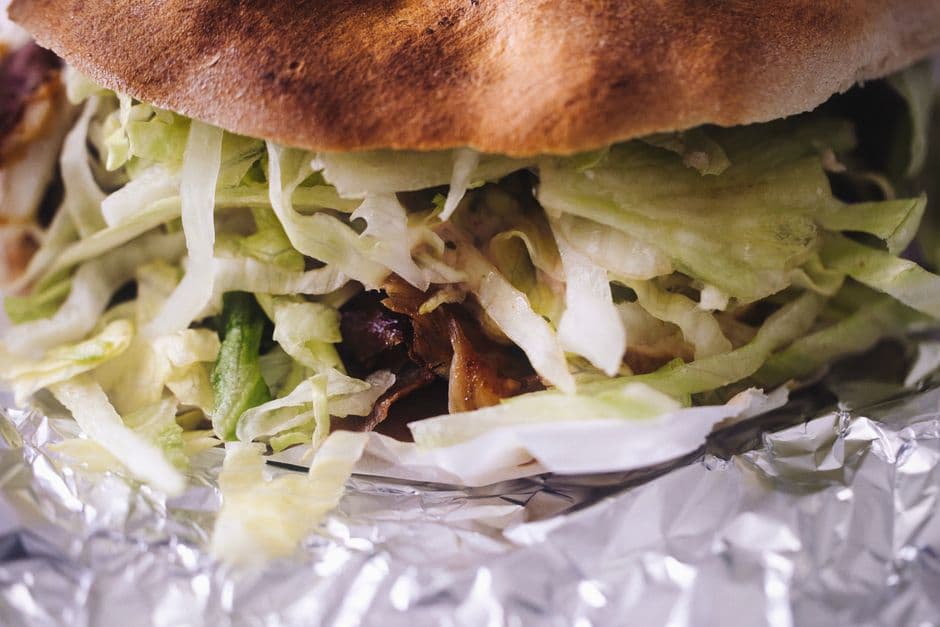 Close-up of a doner kebab: shaved meat and shredded lettuce inside toasted flatbread, wrapped in foil