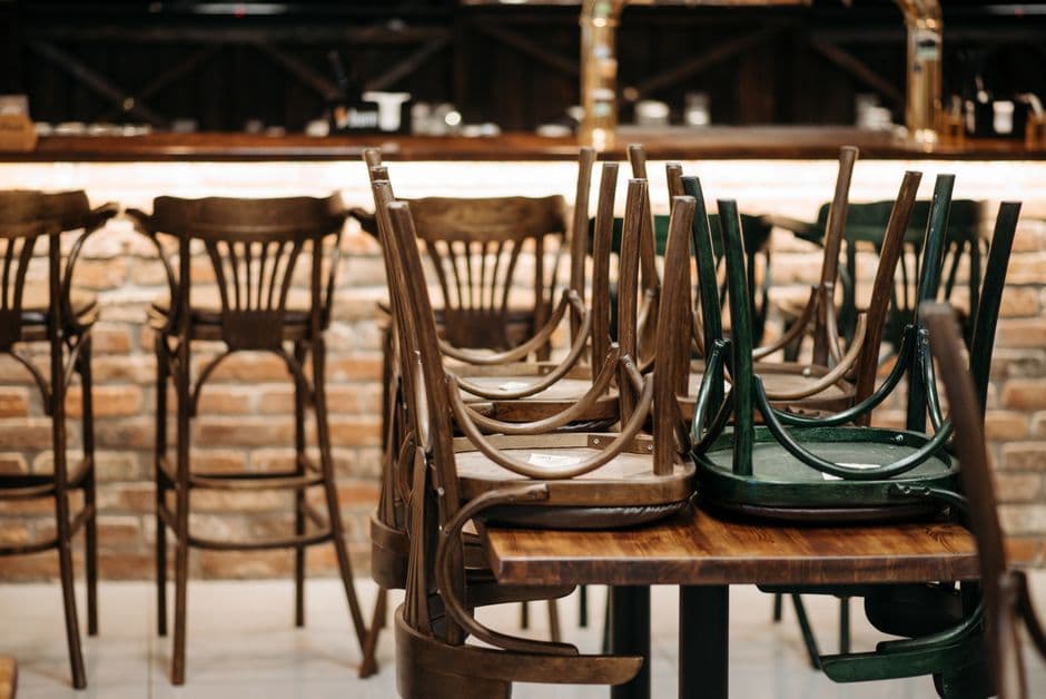 Wooden chairs stacked upside down on tables in a closed restaurant in front of an empty bar