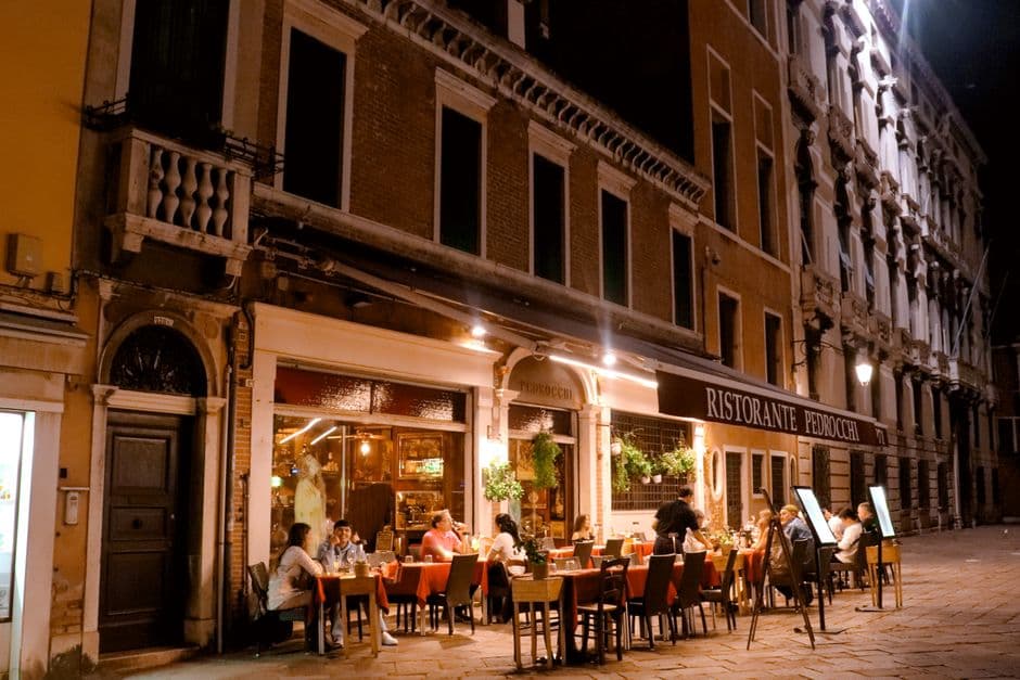 Diners eating at outdoor tables under the awning of Ristorante Pedrocchi in Italy on a warm evening
