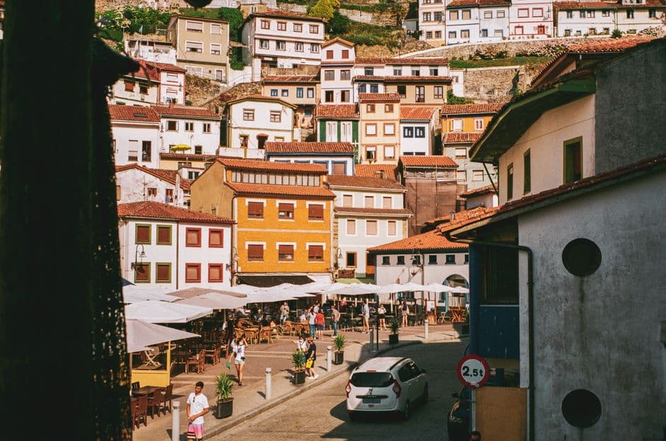 The harbor square in Cudillero, Asturias, in northern Spain, lined with restaurant terraces and parasols on a summer afternoon