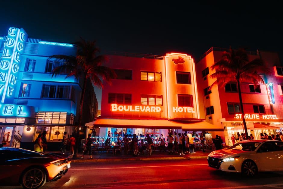 The neon lit Colony, Boulevard and Starlite hotels on Ocean Drive in Miami Beach at night, with sidewalk dining tables full