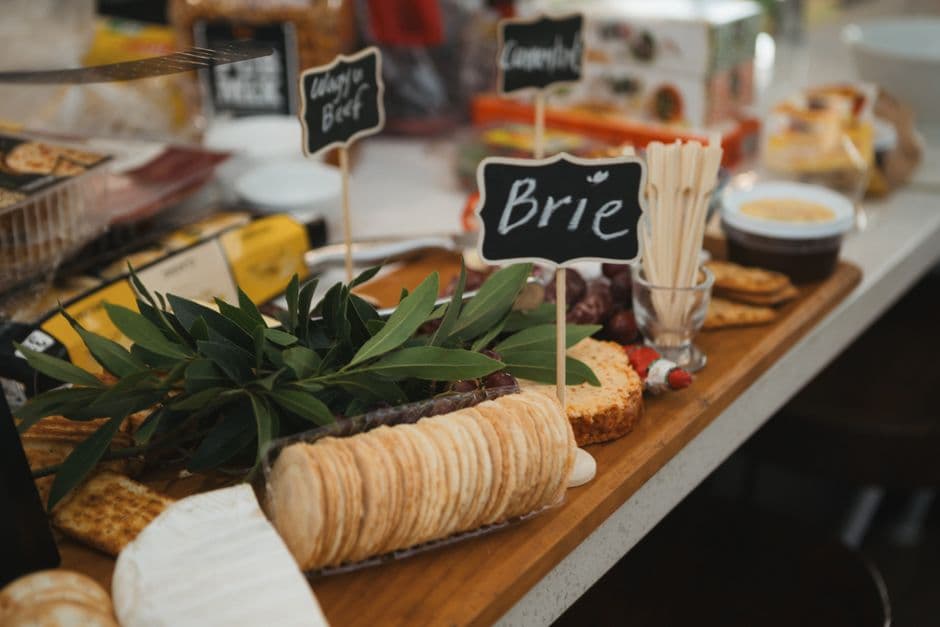 A cheese and cracker board with a chalkboard label reading Brie, set out with olive branches and wooden picks