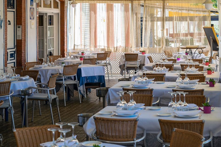 An empty outdoor restaurant terrace with wicker chairs and tables set with white cloths and upturned glasses