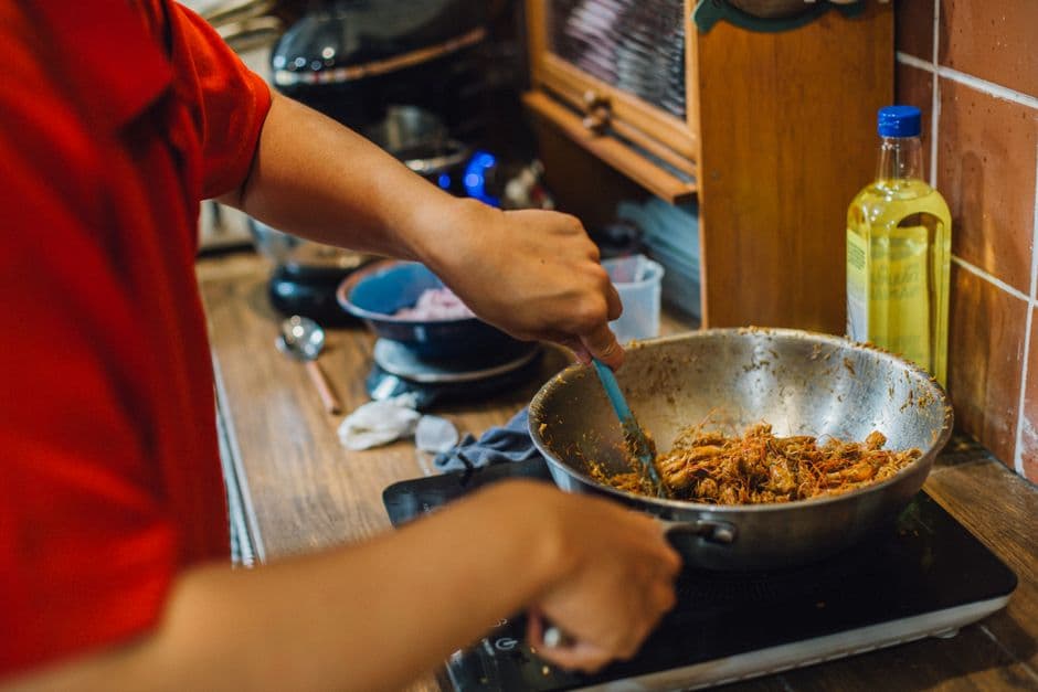 A cook stirring a spiced shredded meat dish in a wok on a portable hob in a home kitchen