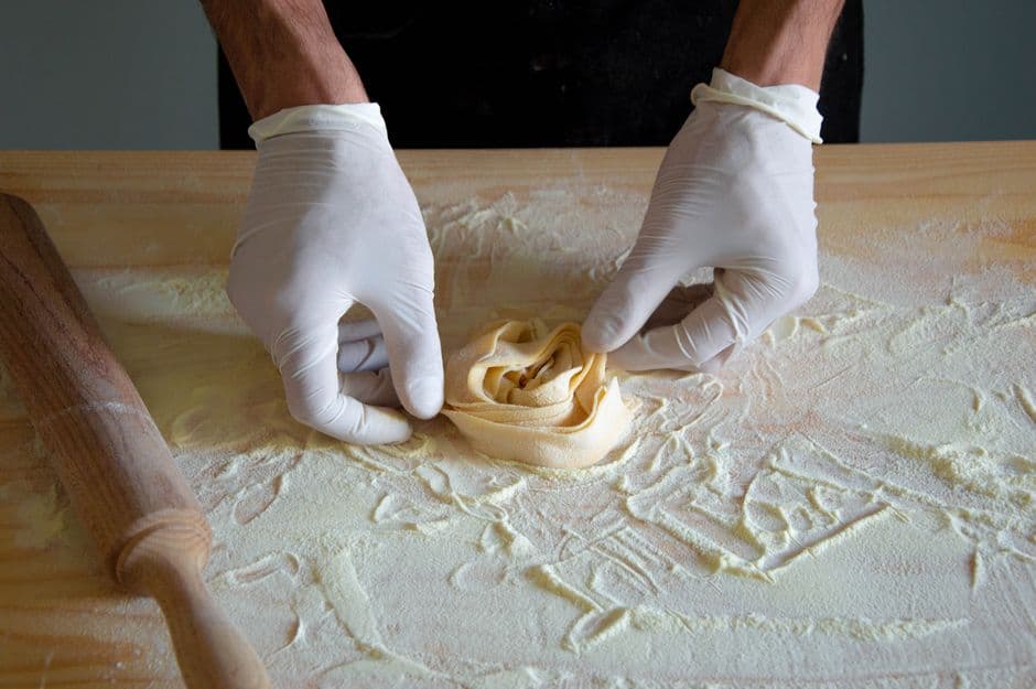 Hands folding a nest of freshly rolled egg pasta on a floured wooden board next to a rolling pin