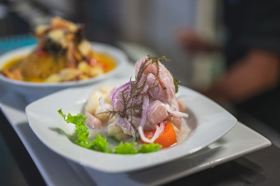 A plate of ceviche with red onion, sweet potato and lettuce being served on a restaurant pass