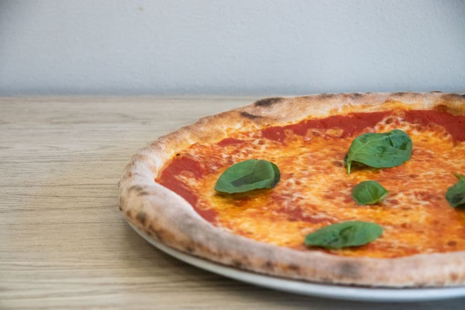 A margherita pizza with a puffed, blistered crust and fresh basil leaves on a plate