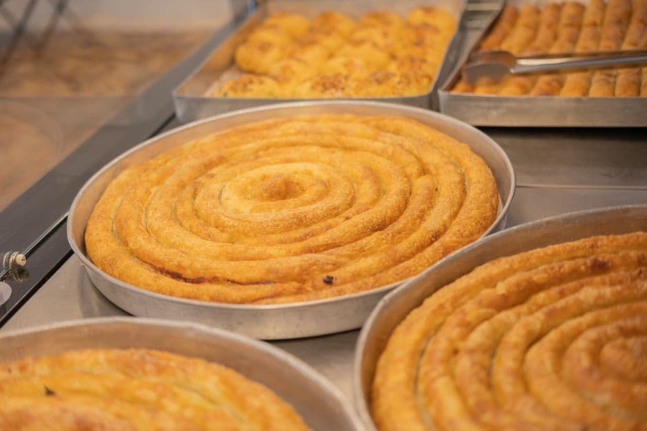 Round metal trays of coiled golden savory pastry on a bakery counter