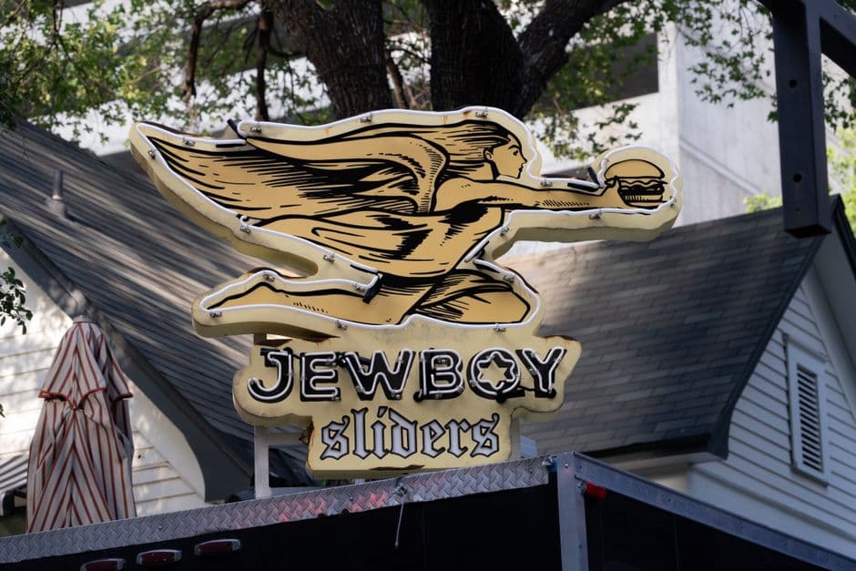 Neon sign for JewBoy Sliders, a burger trailer in Austin, Texas, mounted above the trailer roof under oak trees