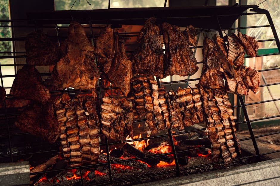 Racks of beef ribs and whole cuts cooking over a wood fire at a traditional Argentine asado