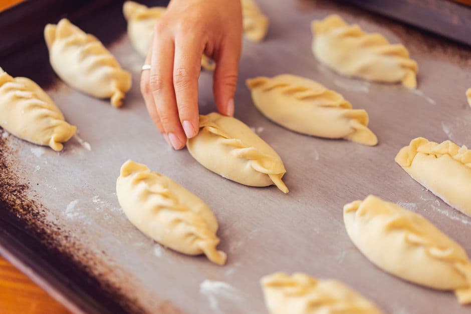 A hand placing raw empanadas with braided crimped edges onto a baking tray