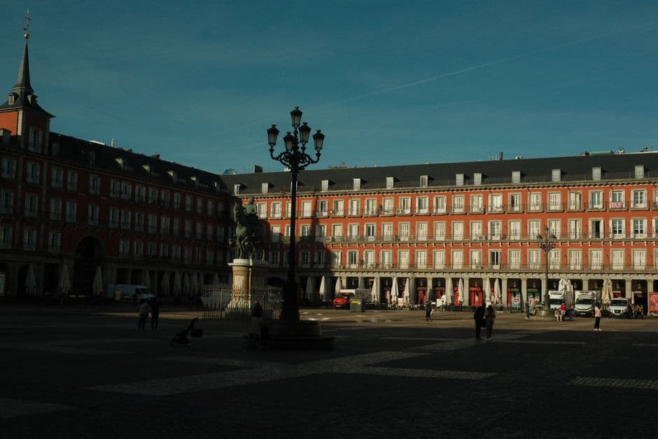 Plaza Mayor in Madrid in low sun, with its red arcaded facades, slate roofs, a wrought iron lamp post and the equestrian statue of Philip III