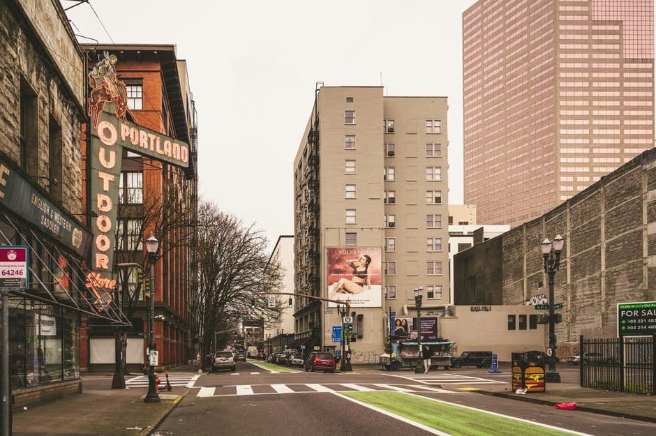 A street in downtown Portland, Oregon with a tall neon sign reading Portland Outdoor Store topped by a rider on a bucking horse, brick buildings and a pink glass tower behind
