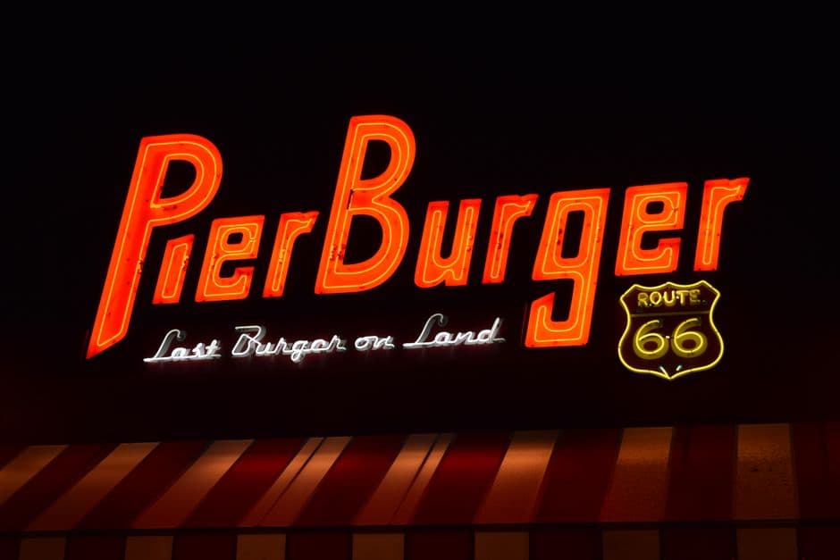 The red neon sign of Pier Burger at night, with the words Last Burger on Land and a yellow Route 66 shield