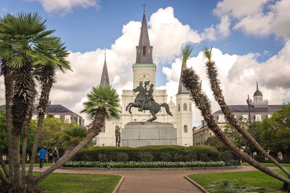 Jackson Square in the New Orleans French Quarter, with the white facade and three spires of St Louis Cathedral behind the Andrew Jackson equestrian statue, framed by palms