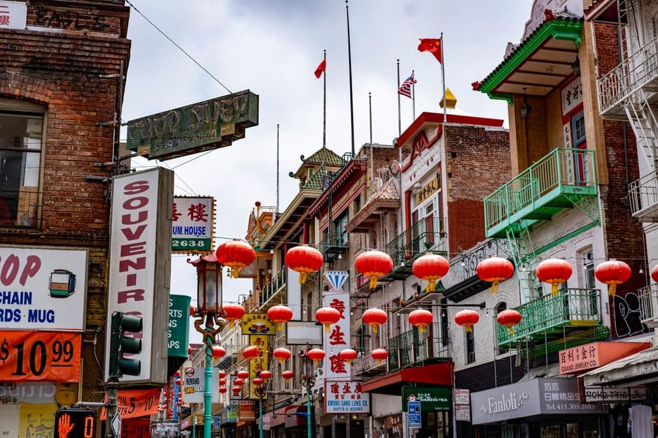 A San Francisco Chinatown street hung with rows of red lanterns, with shop signs in Chinese and English above the sidewalk