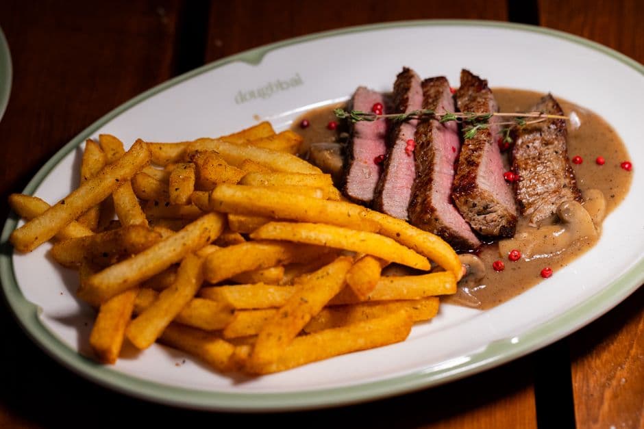 Sliced steak served rare in a peppercorn cream sauce with a heap of fries on an oval plate