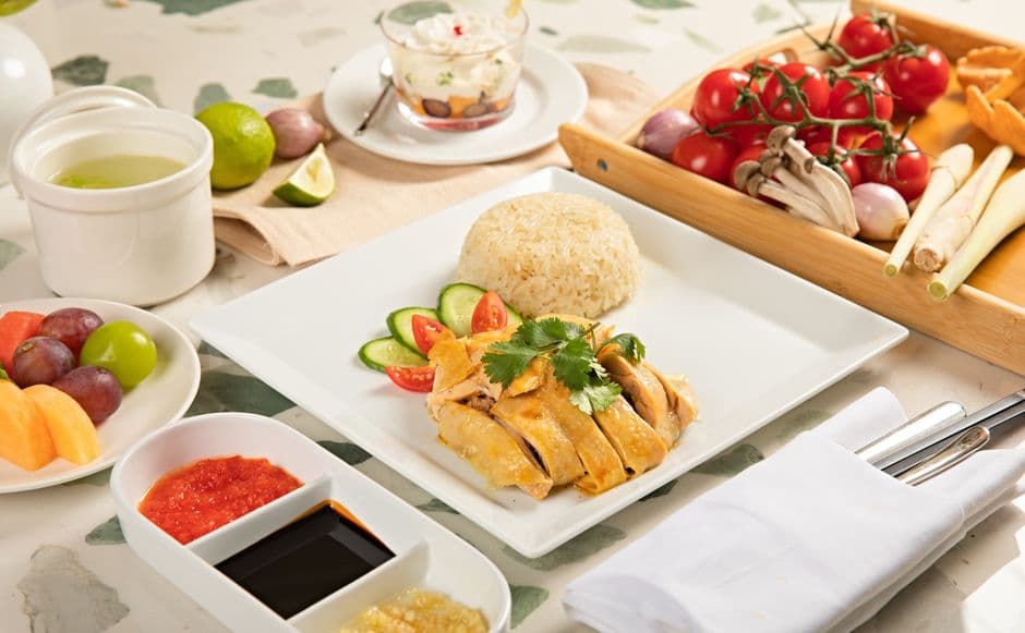 A plate of chicken rice: sliced poached chicken beside a mound of rice, with chili sauce, dark soy sauce and minced ginger in a divided dish