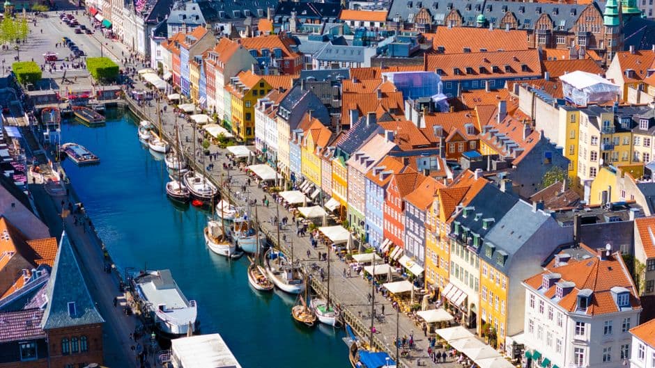 Aerial view of the Nyhavn canal in Copenhagen, lined with colorful townhouses, wooden boats and quayside restaurant awnings