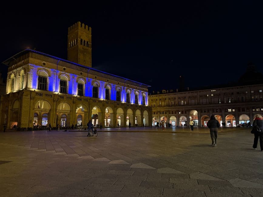 Piazza Maggiore in Bologna at night with the Palazzo del Podesta lit up and the porticoes of the square glowing behind