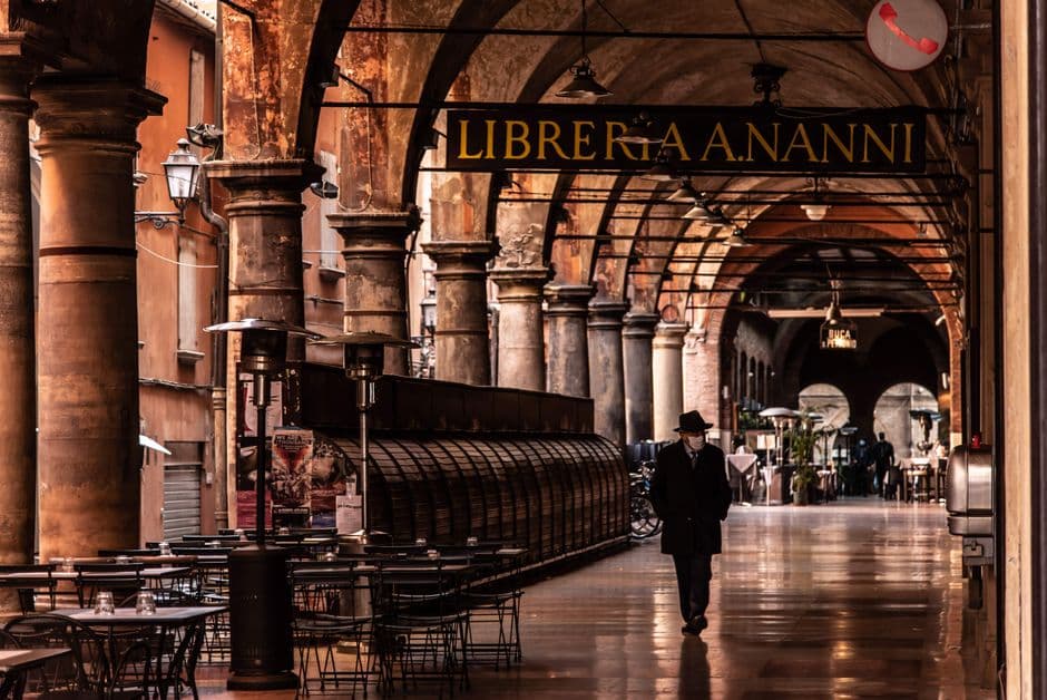 A covered portico in central Bologna with restaurant tables set out under the arches and a gold Libreria A. Nanni sign overhead