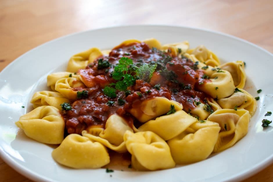 A white plate ringed with large filled pasta parcels around a pool of tomato sauce and chopped herbs